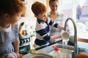 Kaksi lasta ja heidän äitinsä pesemässä astioita