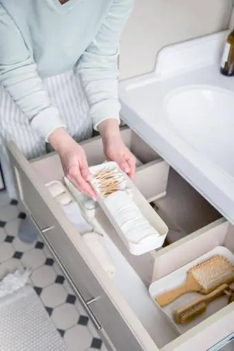 ქალი აწყობს ტუალეტის პროდუქტებს აბაზანაში უჯრაში