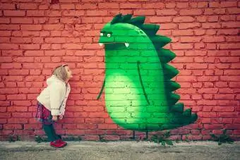 Mladá dívka s úsměvem na imaginární monstrum přítele namalované na zdi