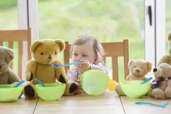 Copil care hrănește ursuleți de pluș la masă