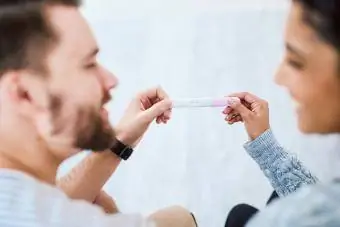 Glückliches junges Paar, das zusammen auf dem Sofa sitzt und einen positiven Schwangerschaftstest in der Hand hält