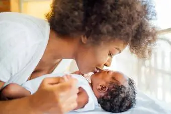 Moeder kust babydochter die thuis op bed ligt