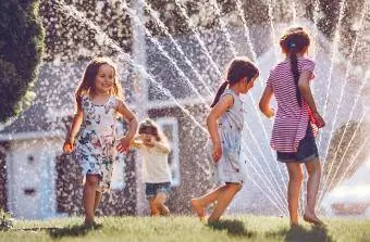 crianças correndo através de um aspersor de água no quintal
