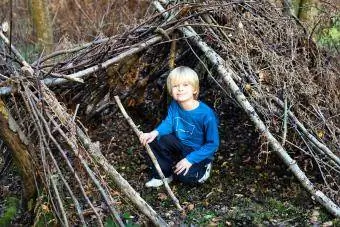 pojke i skogen med fort den gjorda av trädgrenar