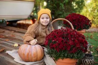 dievča na verande s tekvicou a kvetinovou výzdobou pre mamičky na jeseň