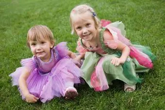 småbarn flickor i älva kostymer sitter på gräs utanför