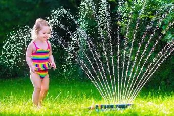 småbarn flicka kör i vatten sprinkler