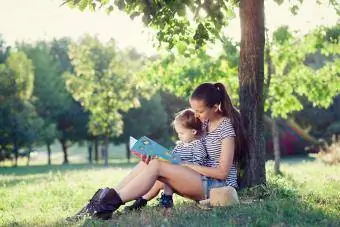 ibu membacakan untuk anak balita di bawah pohon
