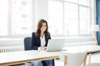 Poslovna ženska sedi za mizo v pisarni in dela na prenosnem računalniku