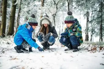 Otroci opazujejo živalske sledi na snegu v zimskem gozdu