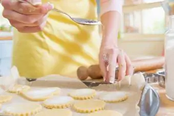 wanita menabur gula pada doh biskut di dapur