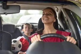 Glad fotballmamma som frakter ungen til fotballtrening i bilen sin
