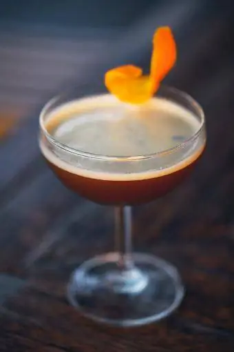 Ciemny koktajl przyozdobiony pomarańczowym akcentem na ciemnym barze