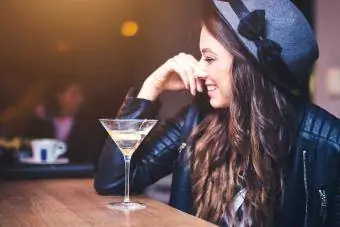 Wanita muda berambut coklat duduk di bar dan menikmati koktel dengan sentuhan lemon