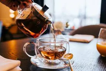 एक स्टाइलिश पारदर्शी चायदानी से हाथ से चाय का कप डालते हुए