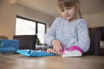 Niño usando cinta adhesiva para asegurar papel de regalo azul alrededor de un regalo