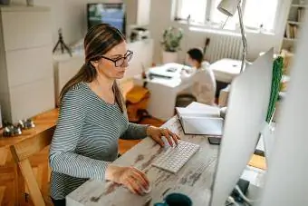 Madre trabajando en la computadora mientras su hijo mira televisión en casa