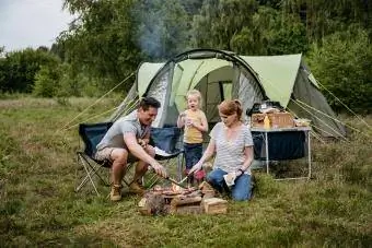 Семейство с едно дете, което готви на открит огън на къмпинг
