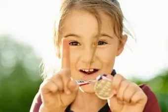 Põnev väike tüdruk näitab oma võidumedalit ja žestikuleerib number üks