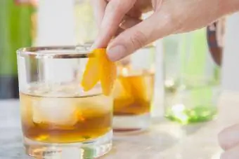 बारटेंडर कॉकटेल ग्लास को संतरे के छिलके से सजाते हुए