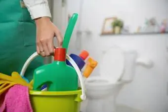 Kvinne står på badet og holder en bøtte full med rengjøringsmidler