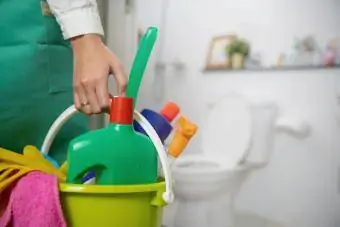 Vrouw staat in de badkamer met een emmer vol schoonmaakmiddelen