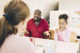 Verbaasde man sit met seun en praat met onderwyser by klaskamer