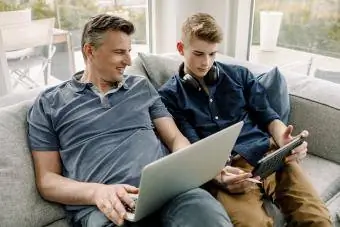 Улыбающийся отец с ноутбуком смотрит на сына с помощью цифрового планшета