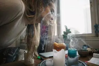 Ung kvinne blåser duftlys på bordet mot vinduet