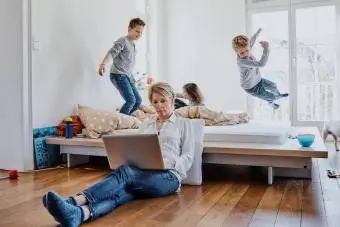 Madre usando una computadora portátil en casa con niños retozando en segundo plano
