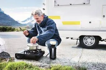 mann som lager mat på turistkomfyr i nærheten av bobil i fjell