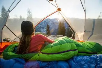 Eine Frau beobachtet den Sonnenaufgang aus einem Zelt.