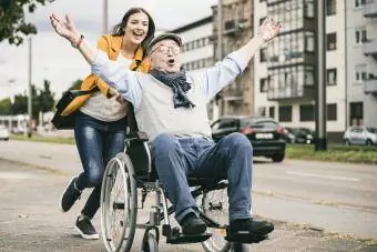 Młoda kobieta pcha starszego mężczyznę na wózku inwalidzkim