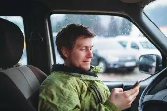 Jeune homme souriant à la veste verte tenant un smartphone dans la voiture