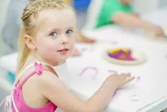 Ένα νεαρό κορίτσι κάθεται σε ένα τραπέζι και ζωγραφίζει με τα δάχτυλα