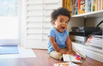 Meglepett kisfiú ül a padlón és játszik a könyvekkel