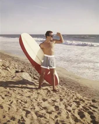 นักโต้คลื่นศิลปะรีโทรถือกระดานโต้คลื่นขณะยืนอยู่บนชายหาด