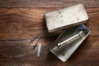 سرنگ شیشه ای قدیمی در یک جعبه فلزی و سوزن روی میز چوبی