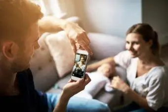 Man neem foto's van sy vrou met hul nuwe baba op 'n foon by die huis