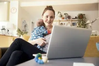 Madre usando una computadora portátil y sosteniendo a su bebé recién nacido en casa