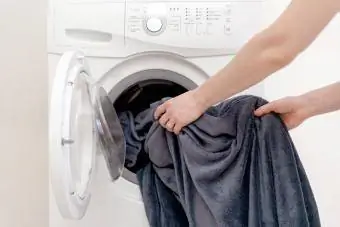 Les mains des femmes mettent le linge dans la machine à laver blanche