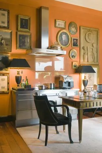 Pomarańczowe ściany „Hermes” i blisko pogrupowane obrazy w kuchni z urządzeniami Gaggenau