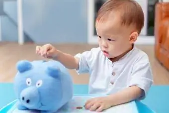 Bayi lelaki kanak-kanak kecil memasukkan syiling ke dalam piggy bank biru