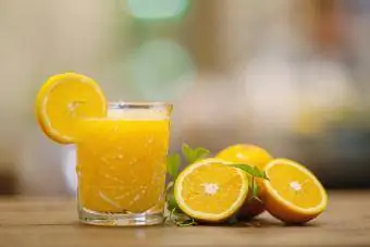 براندی و آب پرتقال تازه در کنار چند تکه پرتقال روی میز چوبی