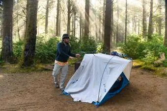 Mann baut Zelt auf Waldcampingplatz auf