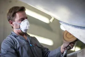 Industriarbeider som har på seg beskyttelsesmaske mens han rengjør metall