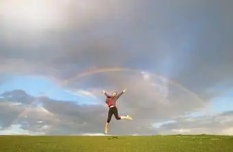 Havada zıplayan kadın, gökyüzündeki Rainbos'un altında Feng Shui'de iyi şanslar kutluyor