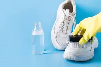 Lastik eldiven giyen kadın beyaz spor ayakkabılarındaki tuz lekelerini fırçayla temizliyor.