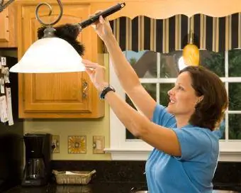 Mujer usando plumero para quitar el polvo de la lámpara de la cocina ahdes