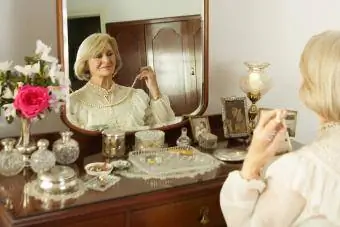 Starija žena sjedi za toaletnim priborom i isprobava ogrlicu